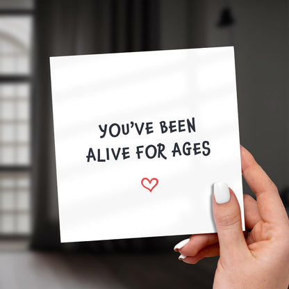 Hand holding a card with 'You've been alive for ages' text and a heart symbol.