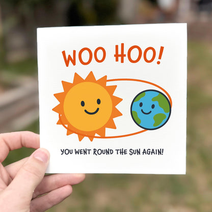 Card with sun and Earth illustration and 'WOO HOO!' text held by a hand.