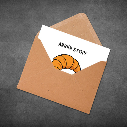 Envelope with a card inside featuring a croissant and text 'AHHHH STOP!' on a dark gray background