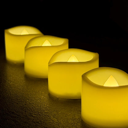 Four yellow candles lined up on a dark surface