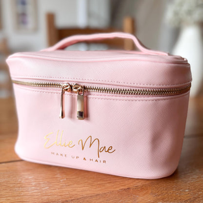 Pink makeup bag with gold zipper and 'Ellie Mae' branding on a wooden surface.