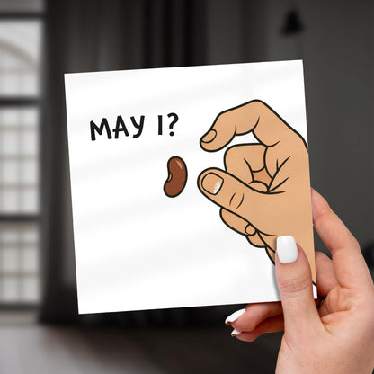 Hand holding a card with a hand holding a walnut and 'May I?' text.