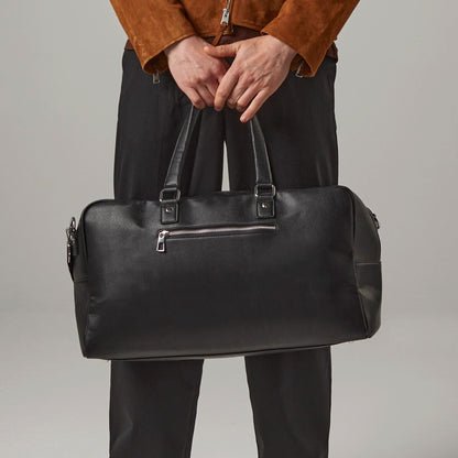 Person holding a black leather duffel bag against a neutral background