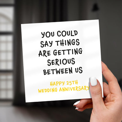 Hand holding a card with humorous 25th wedding anniversary message.