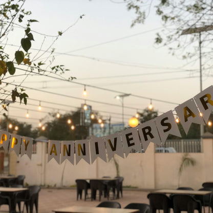 Decorative 'Happy Anniversary' banner hanging outdoors with tables and chairs in the background.