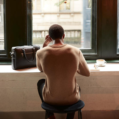 Man sitting by a window with a suitcase and coffee cup, looking out.