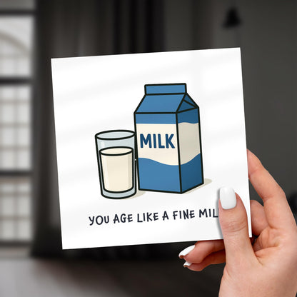 Card with a milk carton and glass illustration and text, held by a hand.