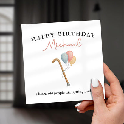 Hand holding a birthday card with balloons and a cane, personalized for 'Michael'.