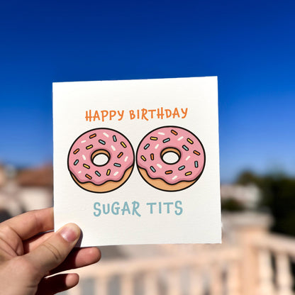 Hand holding a birthday card with pink donuts and text against a blue sky.