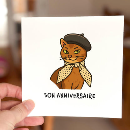Card with a cat illustration and 'Bon Anniversaire' text held by a hand.