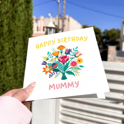 Hand holding a birthday card with flowers and 'Happy Birthday Mummy' text outdoors.