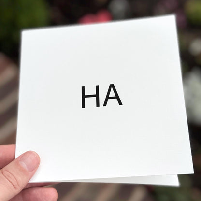 White square card with 'HA' printed on it held by a hand against a blurred background
