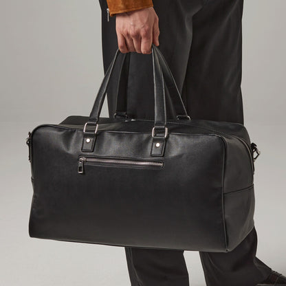 Person holding a black duffel bag against a neutral background