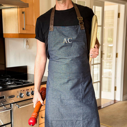 Person wearing a blue apron with 'AC' monogram, holding a pizza peel in a kitchen.