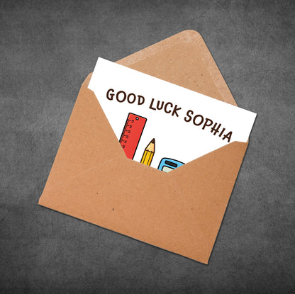 Brown envelope with a card inside reading 'Good Luck Sophia' on a dark gray background