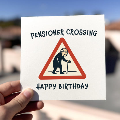 Birthday card with 'Pensioner Crossing' design held by a hand outdoors.