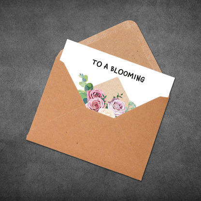 Greeting card with floral design and text 'To a Blooming' inside an open brown envelope on a dark background.