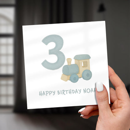 Hand holding a birthday card with a train and number 3 design.