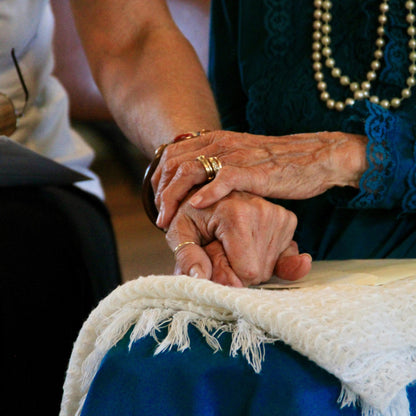 Close-up of two pairs of hands holding each other, with a focus on the interwoven fingers.