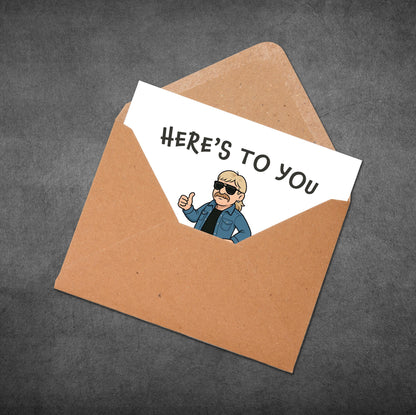 Card with a cartoon character and 'Here's to you' text in an open brown envelope on a dark gray background