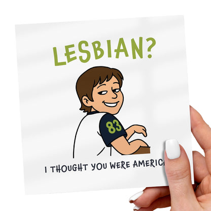 Card with cartoon character and text 'LESBIAN? I Thought You Were American' held by a hand.