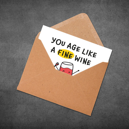 Envelope with a card inside that reads 'You age like a fine wine' on a gray background
