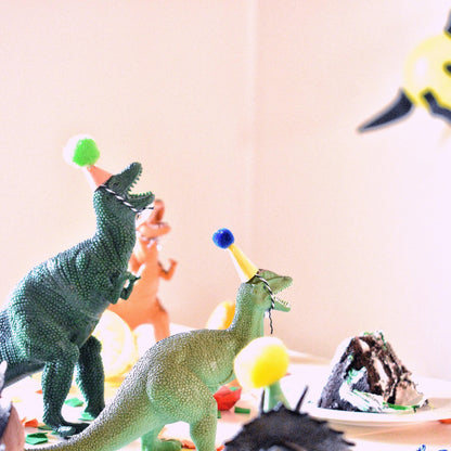 Two toy dinosaurs with party hats on a table with a blurred background