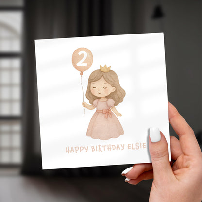 Hand holding a birthday card with an illustration of a girl in a dress and a number two balloon, with 'Happy Birthday Elsie' text.