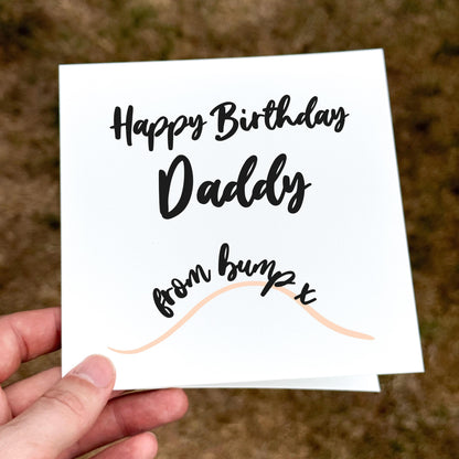 Hand holding a birthday card for 'Daddy from bump x' on a blurred background