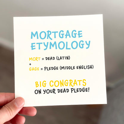 Hand holding a card with 'Mortgage Etymology' text and humorous definition.