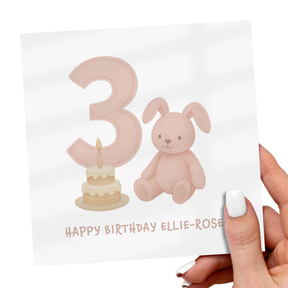 Hand holding a birthday card with a number 3, rabbit, and cake illustration.