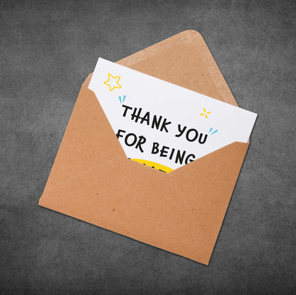Brown envelope with a white card inside that says 'Thank you for being' on a dark gray background