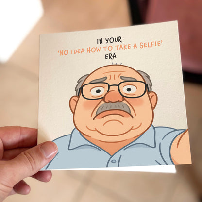 Card with cartoon character holding a selfie stick and text 'In your no idea how to take a selfie era' held by a hand.