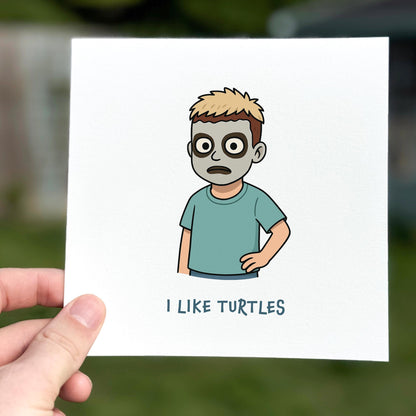 Cartoon character holding a card with 'I LIKE TURTLES' text, held by a hand against a blurred outdoor background.