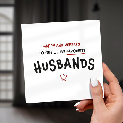 Hand holding a card with 'Happy Anniversary to one of my favourite husbands' text.