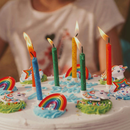 Birthday cake with lit candles and rainbow decorations on a wooden table.