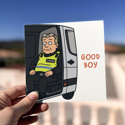 Cartoon police officer in a van with 'GOOD BOY' text, held by a hand against a blurred outdoor background.