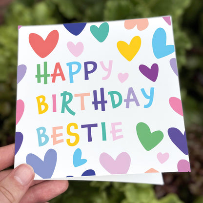 Hand holding a small square card with colorful hearts and 'Happy Birthday Bestie' text.