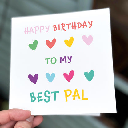 Hand holding a birthday card with colorful hearts and text.