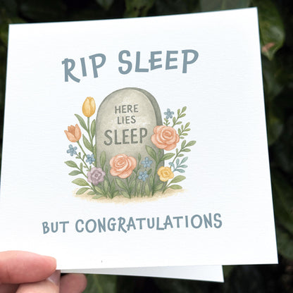 Card with tombstone illustration and humorous text 'RIP SLEEP HERE LIES SLEEP BUT CONGRATULATIONS' held by a hand.