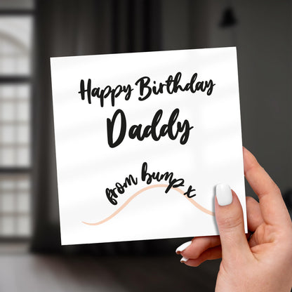 Hand holding a birthday card for 'Daddy' with decorative text on a blurred background