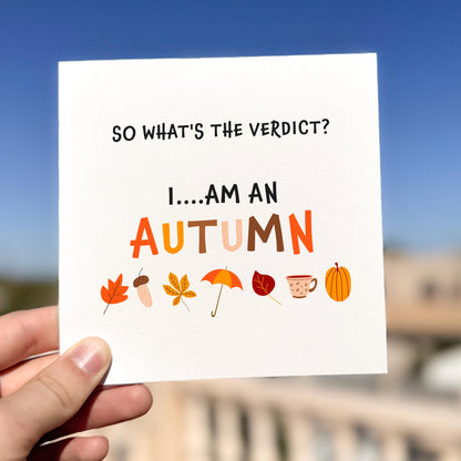 Hand holding a card with autumn-themed text and icons against a blurred outdoor background
