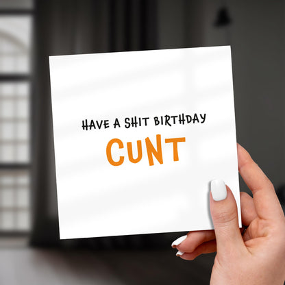 Hand holding a card with offensive text against a blurred background