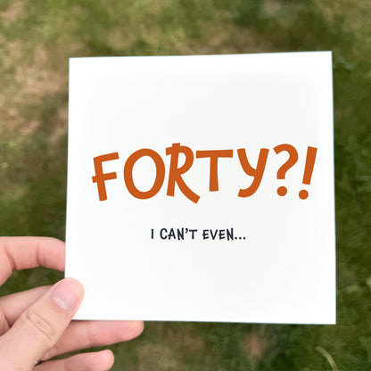 Hand holding a card with 'FORTY?! I CAN'T EVEN...' text against a grassy background
