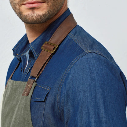 Person wearing a blue denim shirt with green apron and brown straps on a light gray background
