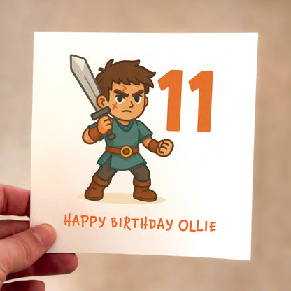 Birthday card with a cartoon character holding a sword and the number 11, held by a hand.