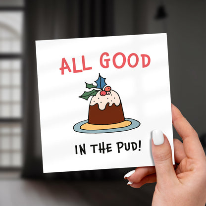 Card with a Christmas pudding illustration and text 'All good in the pud!' held by a hand.