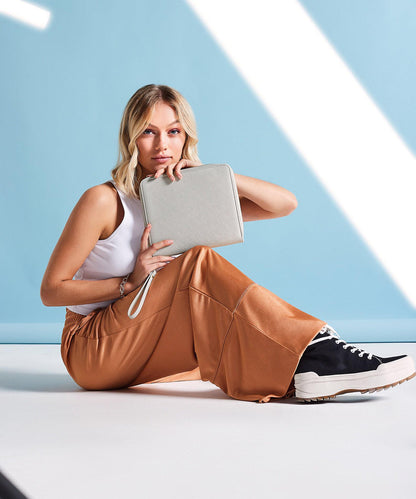 Woman sitting on a white surface holding a gray clutch against a light blue geometric background