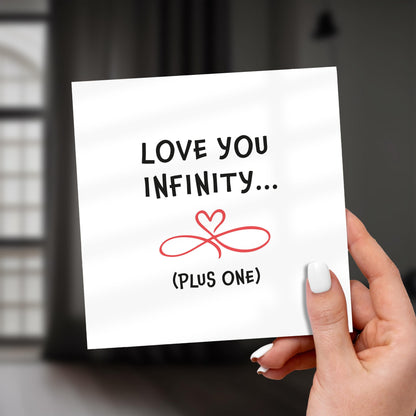 Hand holding a card with 'Love you infinity... (plus one)' text and heart design.