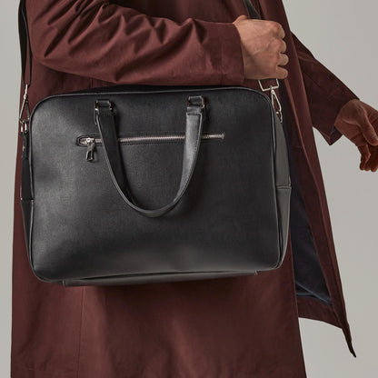 Person holding a black leather briefcase against a neutral background